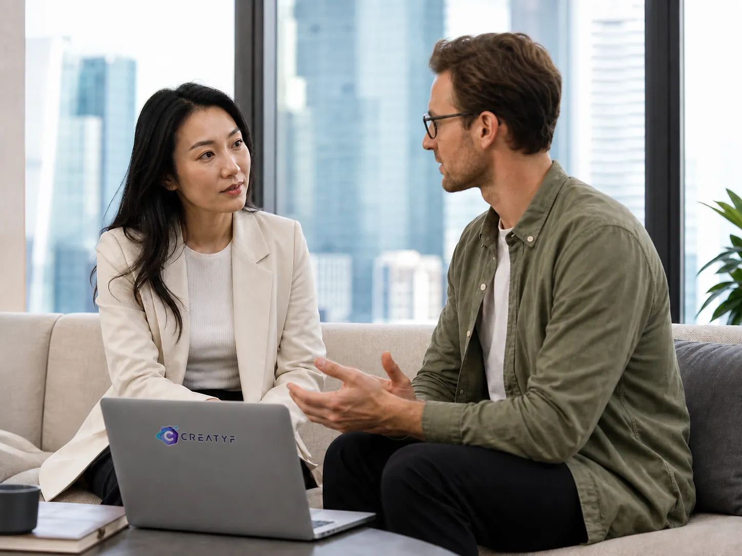 Illustrative editorial scene of two fictional international professionals talking in an office lounge with a city view.